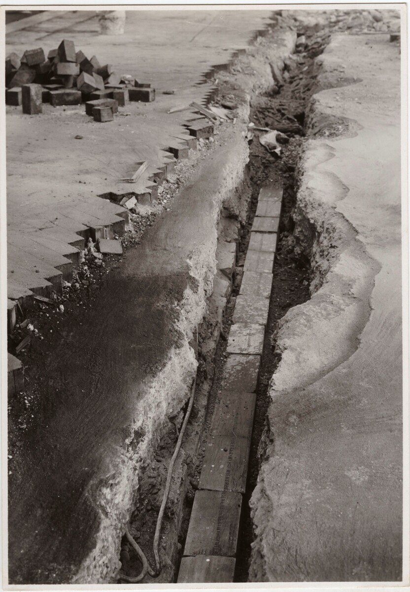 Schwarzes und weißes Foto einer gebrochenen Straße mit verstreuten Ziegeln auf der linken Seite.