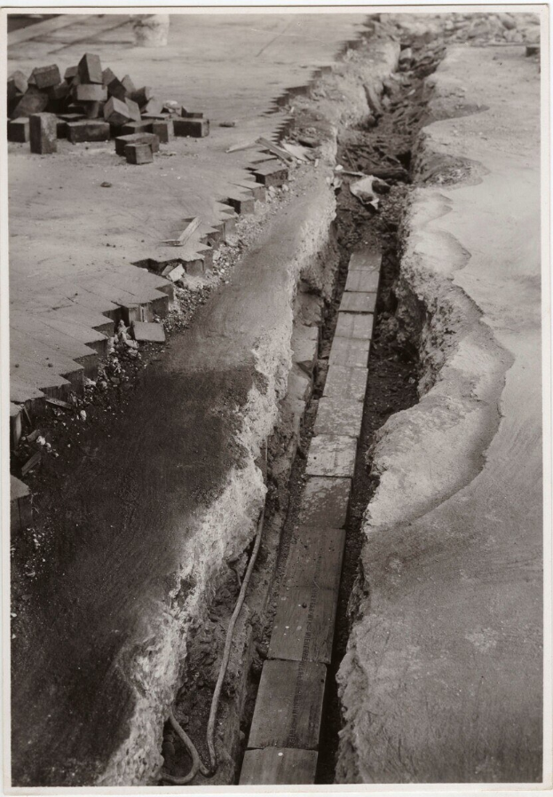 Schwarzes und weißes Foto einer gebrochenen Straße mit verstreuten Ziegeln auf der linken Seite.