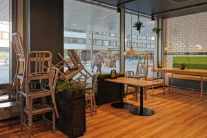 Ein Restaurantinnenraum mit Holztischen und -stühlen, große Fenster mit Blick auf eine belebte Straße in Berlin, Deutschland, umgeben von Pflanzen und Dekolights.