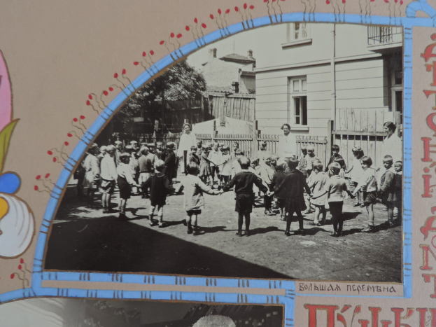 Schwarz-weißes Foto von Kindern, die in einer Straße mit Gebäuden, Bäumen und einem Zaun im Hintergrund spielen.