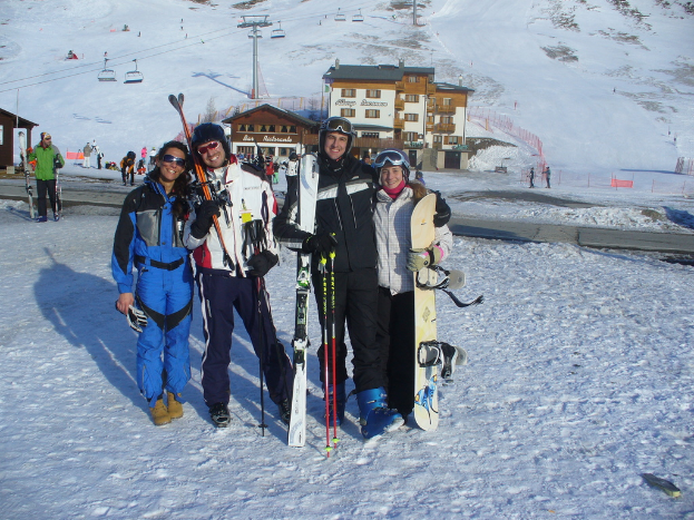 Vier Personen posieren für ein Foto mit Skating Pads und Werkzeugen, mit Gebäuden und anderen Menschen im Hintergrund, vor einer schneebedeckten und eisigen Berglandschaft.
