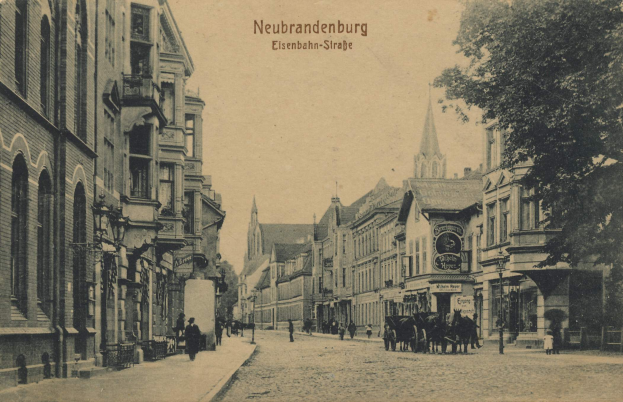 Ein schwarz-weißes Foto einer Stadtstraße in Neubrandenburg, Deutschland, mit Menschen, einem Pferdewagen, Gebäuden mit Fenstern, Schildern, Straßenlaternen, einem Baum und einem bewölkten Himmel.