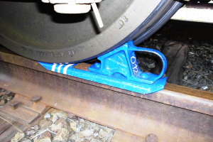 Ein Nahaufnahme eines Zugrades auf einer Schiene mit einer blauen Bremse daran, umgeben von Steinen.