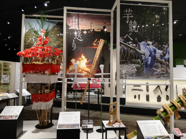 Ein Raum voller verschiedener Gegenstände auf einem Stand, darunter Schilder mit Text, Stände und andere Gegenstände, mit Schildern mit Bildern und Text sowie Deckenleuchten, die eine festliche Atmosphäre für die Tokyo Toy Fair 2019 schaffen.
