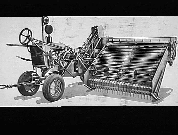 Schwarzes und weißes Foto eines Traktors mit einem angebauten Mähdrescher, der ein großes Vorderrad und ein kleineres Hinterrad hat.