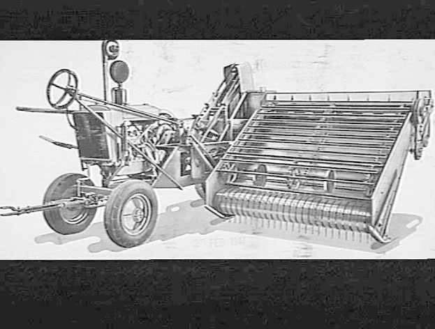 Schwarzes und weißes Foto eines Traktors mit einem angebauten Mähdrescher, der ein großes Vorderrad und ein kleineres Hinterrad hat.