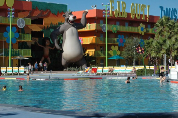 Ein Schwimmbad mit blauem Wasser und Menschen, die darin schwimmen, mit entfernten Cartoons und Stangen im Hintergrund.