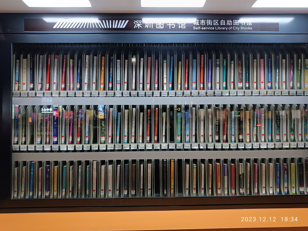 Eine gut beleuchtete Bibliothek mit hohen Bücherregalen voller Bücher, mit einer Tafel mit Text und einem Wasserzeichen unten, das an eine Selbstbedienungsbibliothek von Stadtblöcken erinnert.