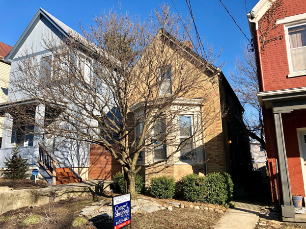 Eine Reihe von Häusern mit einem Baum davor, umgeben von Pflanzen, Gras und Steinen, mit einem Schild, auf dem "Mietwohnungen zur Vermietung, Listid 29058910, Lage 5901 S Elmwood Ave Chicago 60618" steht, unter einem Himmel mit Drähten, die entlang der Oberseite verlaufen.