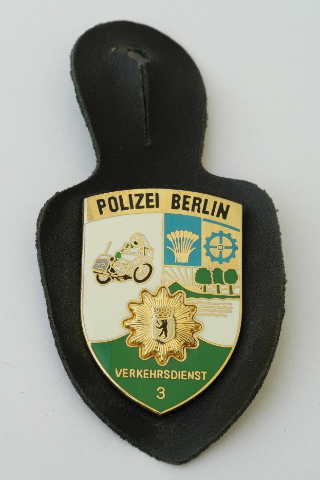 Ein schildförmiges Polizeibadged mit "Polizei Berlin" in schwarzer fetter Schrift auf einem blauen Hintergrund mit einem weißen Stern und Rahmen, das auf einer Oberfläche liegt.