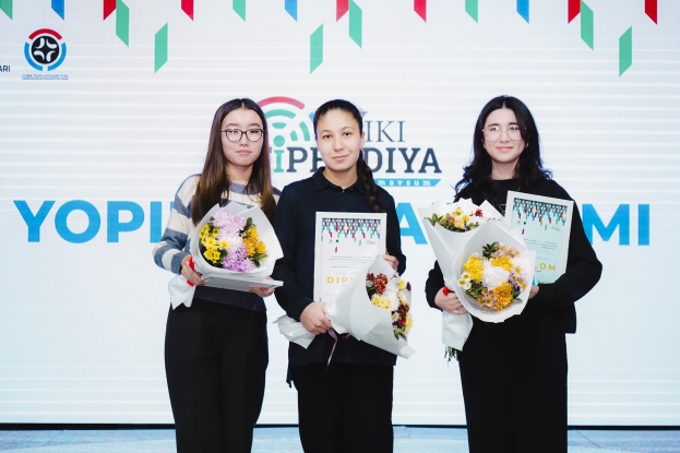 Drei Frauen stehen nebeneinander auf einer Bühne, jede hält einen Blumenstrauß und Zertifikate in den Händen, im Hintergrund ist ein Banner mit der Aufschrift "Yopi Diya Awards 2019" zu sehen.