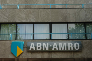 Ein Gebäude mit einer Tafel, auf der "ABN AMRO" steht, mit einer Tafel, die es als Hauptsitz angibt, einem Geländer und Glasfenstern mit Vorhängen, mit Text am unteren Rand, der eine Strafe von 1,5 Milliarden Dollar durch die Europäische Union erwähnt.